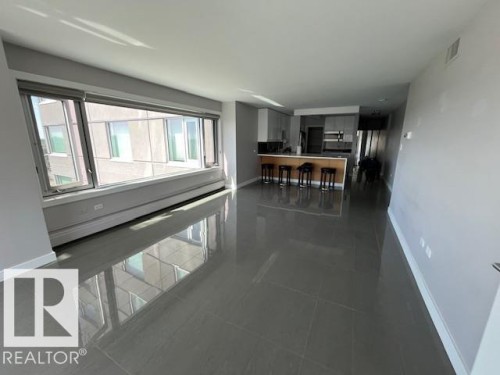 Open-concept living space featuring expansive windows, large format tile flooring, a kitchen with light-toned cabinetry, and a peninsula with bar seating - 1101 10011 123 Street, Edmonton, AB 
