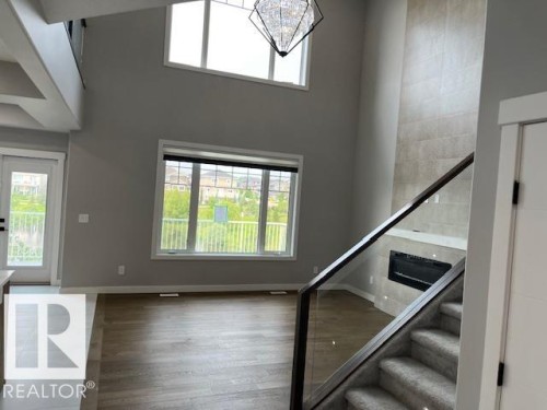 Two-story living area featuring a prominent fireplace with floor-to-ceiling tile surround, a modern chandelier, and large windows with a transomed upper window - 3810 46 Avenue, Beaumont, AB 