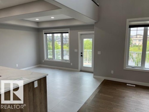 Open concept living area featuring a coffered ceiling with recessed lighting, large windows, a glass-panel door, and a kitchen island with a light-toned countertop - 3810 46 Avenue, Beaumont, AB 