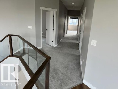 Upper-level hallway featuring a glass and wood-finish railing, light gray carpeting, and recessed lighting - 3810 46 Avenue, Beaumont, AB 