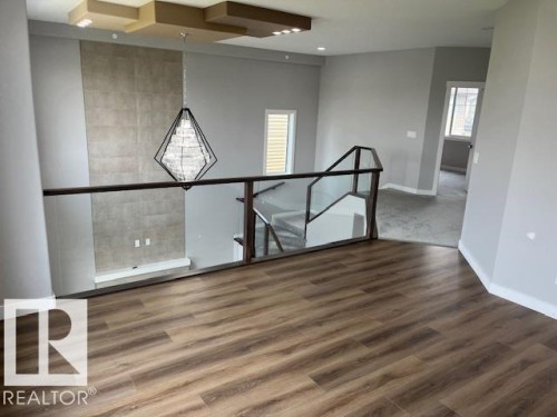 Open concept upper level featuring wood-finish flooring, a contemporary chandelier, a glass and wood railing, and a textured accent wall with a built-in shelf - 3810 46 Avenue, Beaumont, AB 