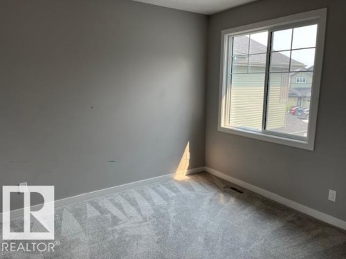 Spacious room featuring light gray walls, white trim, a large window with white framing, and patterned gray carpeting - 3810 46 Avenue, Beaumont, AB 