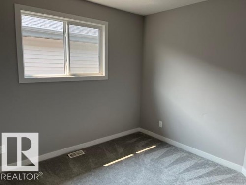 Neutral gray walls featuring white baseboards, a white-framed sliding window, and gray patterned carpet - 3810 46 Avenue, Beaumont, AB 