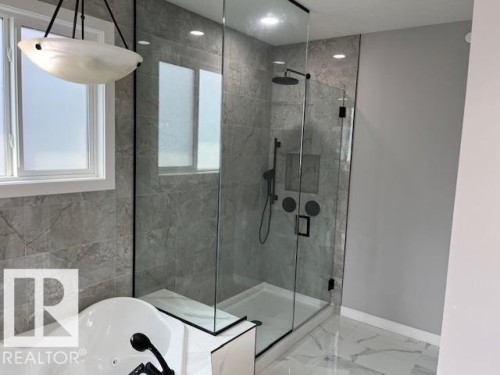 Contemporary bathroom featuring a spacious glass-enclosed shower with matte black fixtures and a built-in niche - 3810 46 Avenue, Beaumont, AB 