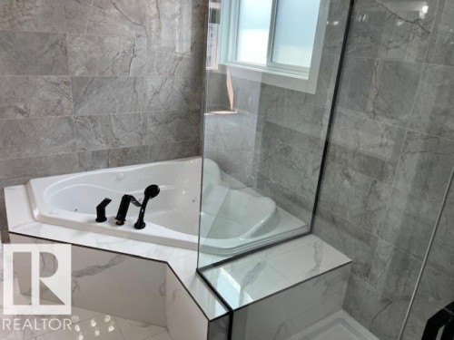 Corner soaking tub with matte black fixtures, set against large-format gray marble-patterned wall tiles - 3810 46 Avenue, Beaumont, AB 