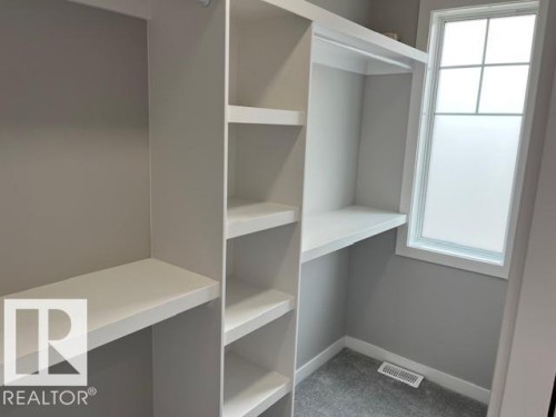 Custom closet system featuring built-in shelving, hanging rods, and a window with frosted panes - 3810 46 Avenue, Beaumont, AB 