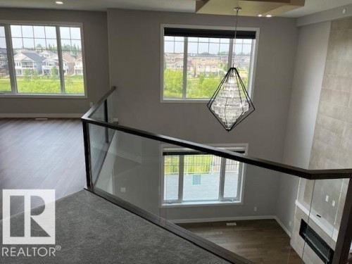 Two-story living area featuring a contemporary chandelier, large windows with white trim, and wood-finish flooring - 3810 46 Avenue, Beaumont, AB 