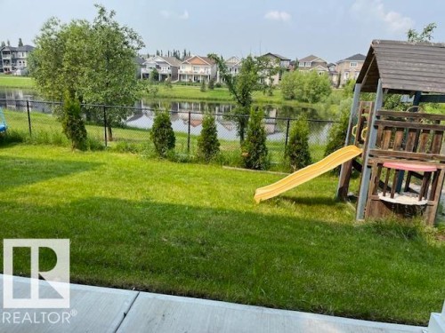 Expansive backyard featuring a manicured lawn, established trees, and a black chain-link fence bordering a pond - 3810 46 Avenue, Beaumont, AB 