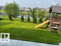 Expansive backyard featuring a manicured lawn, established trees, and a black chain-link fence bordering a pond - 3810 46 Avenue, Beaumont, AB 