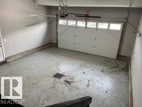 Spacious garage featuring an epoxy-coated floor with integrated drainage, a white paneled overhead door with windows, and light grey painted walls - 3810 46 Avenue, Beaumont, AB 