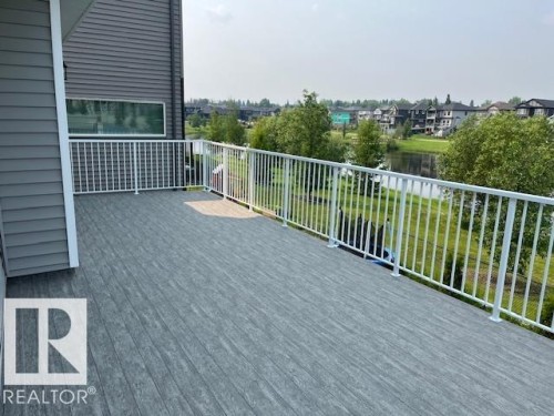 Expansive deck featuring wood-look composite decking and white metal railings overlooking a serene pond - 3810 46 Avenue, Beaumont, AB 