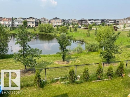Expansive green space featuring a pond and mature trees, bordered by a black chain-link fence - 3810 46 Avenue, Beaumont, AB 