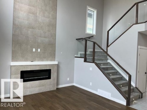 Contemporary living space featuring an expansive fireplace wall with light-toned rectangular tile, a sleek linear electric fireplace, and a white mantel - 3810 46 Avenue, Beaumont, AB 