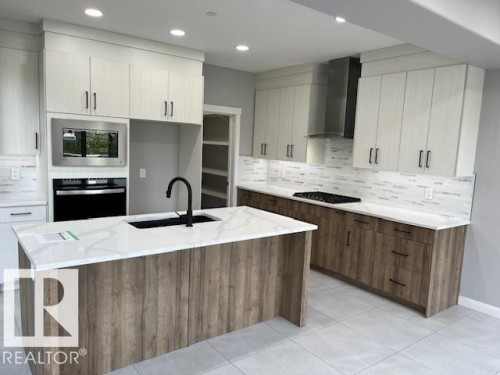 Open-concept kitchen featuring an island with a built-in sink, white countertops, two-tone cabinetry, stainless steel appliances, and tile flooring - 3810 46 Avenue, Beaumont, AB 