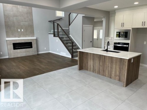 Open-concept living space featuring a wood-finish kitchen island with an undermount sink, quartz countertop, and matte black faucet - 3810 46 Avenue, Beaumont, AB 
