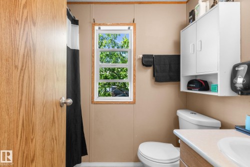 Bathroom featuring a wood-finish door, white paneled window with wood trim, wall-mounted storage cabinet, and a white toilet - 31 Graywood Cove, Stony Plain, AB 