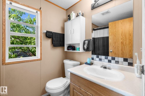 Bathroom featuring a single-pane window with wood trim, a wall-mounted towel bar, a vanity with an integrated sink and wood-finish cabinetry, a toilet, and a medicine cabinet - 31 Graywood Cove, Stony Plain, AB 