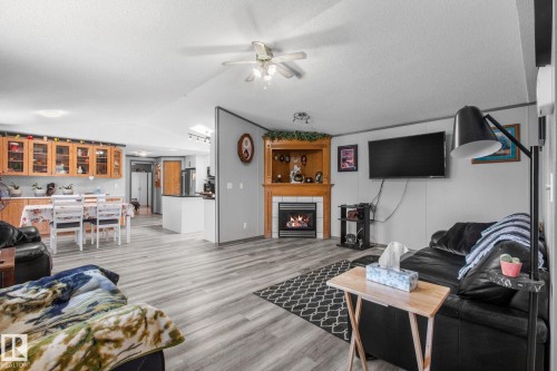 Open-concept living space featuring wood-finish flooring, a built-in fireplace with a wooden mantel, and a ceiling fan - 31 Graywood Cove, Stony Plain, AB 