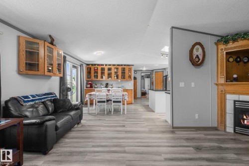 Open-concept living area with wood-finish flooring, a built-in fireplace featuring a tile surround and wood mantel, light gray wall paint, and a skylight providing overhead illumination - 31 Graywood Cove, Stony Plain, AB 