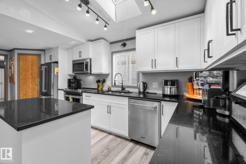 Modern kitchen featuring white shaker cabinetry, dark countertops, stainless steel appliances, and wood-finish flooring - 31 Graywood Cove, Stony Plain, AB 