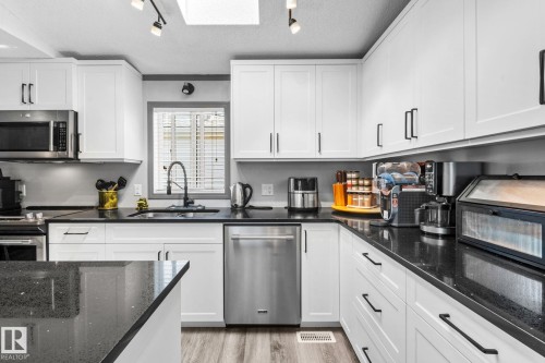 Kitchen featuring white shaker-style cabinetry, dark speckled countertops, stainless steel appliances, and wood-finish flooring - 31 Graywood Cove, Stony Plain, AB 