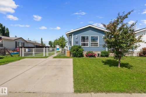 Blue siding exterior with white trim, featuring a concrete driveway, a chain-link fence, and a green lawn with mature trees and shrubbery - 31 Graywood Cove, Stony Plain, AB 