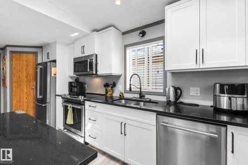 Modern kitchen featuring white shaker cabinetry, stainless steel appliances, dark countertops, a large kitchen island, and a window with blinds - 31 Graywood Cove, Stony Plain, AB 