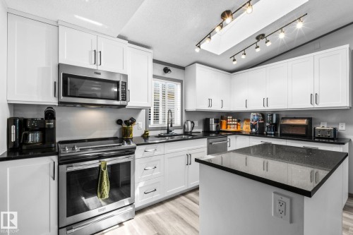Modern kitchen featuring white shaker cabinetry, stainless steel appliances, dark stone countertops, and wood-finish flooring - 31 Graywood Cove, Stony Plain, AB 
