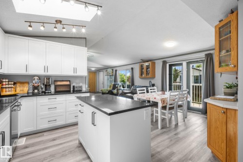 Kitchen featuring white cabinetry with black hardware, dark countertops, a central island, and wood-finish flooring - 31 Graywood Cove, Stony Plain, AB 