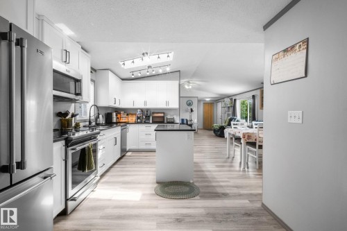 Kitchen featuring white cabinetry, black countertops, stainless steel appliances, and wood-finish flooring - 31 Graywood Cove, Stony Plain, AB 