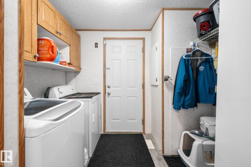 Dedicated laundry area featuring overhead wood cabinetry and a white utility shelf - 31 Graywood Cove, Stony Plain, AB 