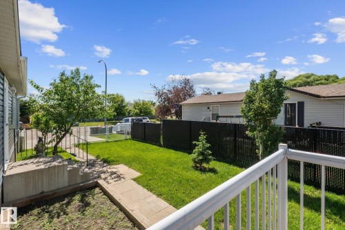 Landscaped front yard featuring a manicured lawn, established trees, and a black chain-link fence - 31 Graywood Cove, Stony Plain, AB 