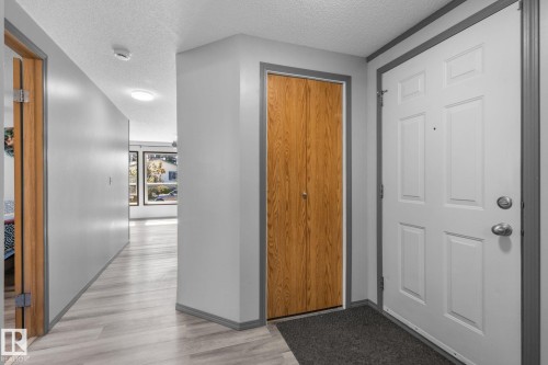 Entryway featuring a paneled door with polished hardware, wood-finish bi-fold closet doors, light wood-finish flooring, and grey trim - 31 Graywood Cove, Stony Plain, AB 