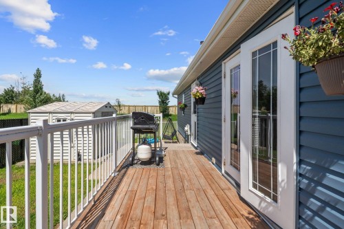 Exterior wood-finish deck with white railings and blue horizontal siding - 31 Graywood Cove, Stony Plain, AB 