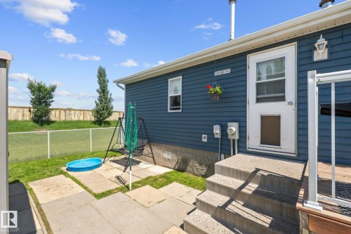Rear exterior featuring blue horizontal siding, concrete steps, and a white screen door - 31 Graywood Cove, Stony Plain, AB 