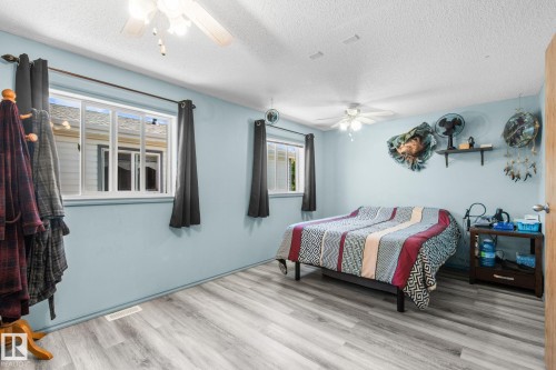 Spacious room featuring light wood-finish flooring, two large windows, and two ceiling fans - 31 Graywood Cove, Stony Plain, AB 