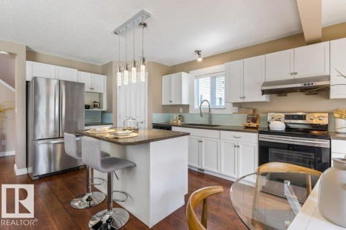 Kitchen featuring white cabinetry, stainless steel appliances, a center island with seating, a tile backsplash, and wood-finish flooring - 1119 Potter Greens, Edmonton, AB - Indoor Photo Showing Kitchen With Upgraded Kitchen