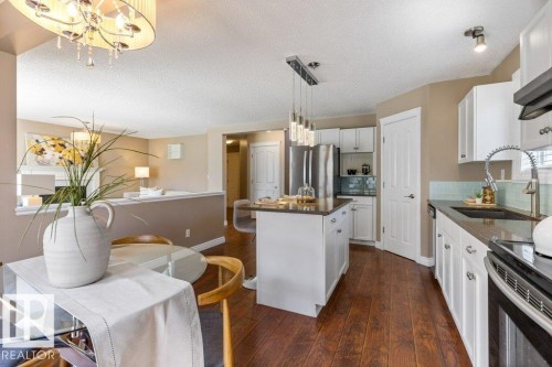Open-concept kitchen and dining area featuring rich wood-finish flooring, white cabinetry, dark countertops, and a subway tile backsplash - 1119 Potter Greens, Edmonton, AB - Indoor Photo Showing Kitchen With Upgraded Kitchen