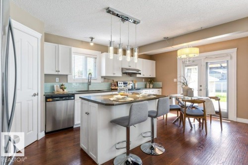 Kitchen featuring white cabinetry, stainless steel appliances, a center island with a dark countertop, and wood-finish flooring - 1119 Potter Greens, Edmonton, AB - Indoor Photo Showing Kitchen With Upgraded Kitchen