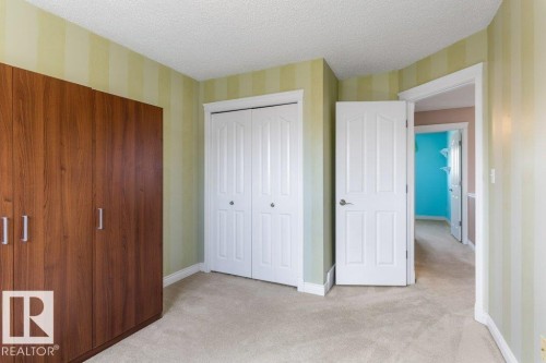 Room featuring soft carpet flooring, a built-in wood-finish wardrobe with silver hardware, and a closet with bifold doors - 1119 Potter Greens, Edmonton, AB - Indoor