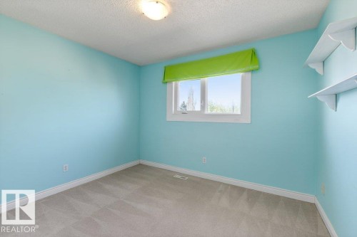Bedroom featuring light blue walls, gray carpet, a white framed window with a green valance, a flush mount ceiling light, and built-in white shelving - 1119 Potter Greens, Edmonton, AB - Indoor Photo Showing Other Room
