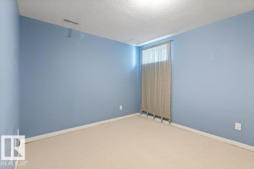 Carpeted room featuring light blue walls, white baseboards, and a window with a patterned curtain - 1119 Potter Greens, Edmonton, AB - Indoor Photo Showing Other Room