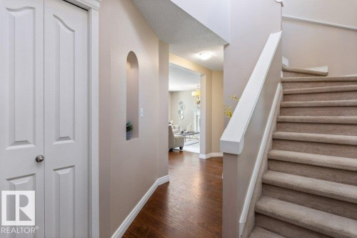 Inviting entryway featuring wood-finish flooring, a carpeted staircase with white railings, a decorative wall niche, and white bi-fold doors - 1119 Potter Greens, Edmonton, AB - Indoor Photo Showing Other Room