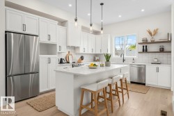 Bright kitchen featuring white shaker cabinetry, stainless steel appliances, a center island with countertop seating, wood-finish flooring, and pendant lighting - 
