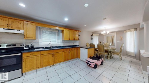 Kitchen area with wood-finish cabinetry, black countertops, and white tile flooring - 3738 28A Street, Edmonton, AB 