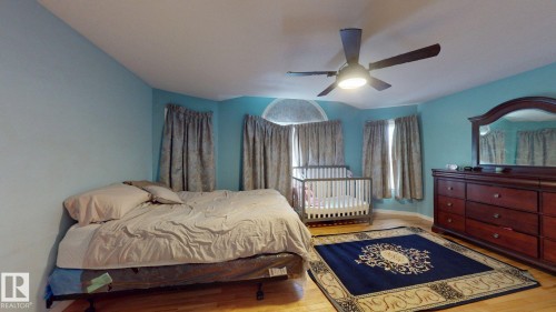 Room featuring wood-finish flooring, a ceiling fan with integrated lighting, and multiple windows with drapery - 3738 28A Street, Edmonton, AB 