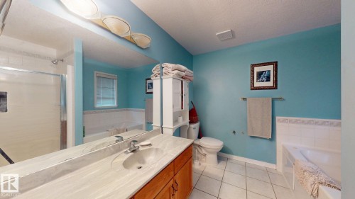 Spacious bathroom featuring a built-in vanity with an integrated sink and wood-finish cabinetry, a large mirror, a shower with a glass enclosure, a built-in bathtub, and ceramic tile flooring - 3738 28A Street, Edmonton, AB 