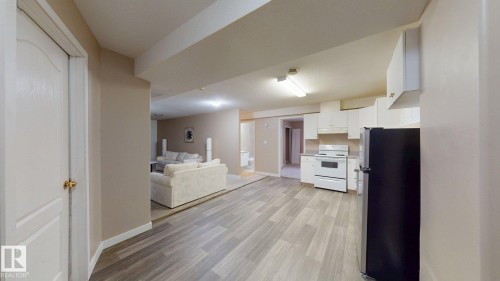 Kitchen area featuring wood-finish flooring, white cabinetry, and white appliances - 3738 28A Street, Edmonton, AB 