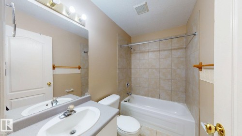 Bathroom featuring a vanity with an integrated sink, a rectangular mirror, a three-bulb light fixture, a toilet, and a bathtub with tile surround - 3738 28A Street, Edmonton, AB 