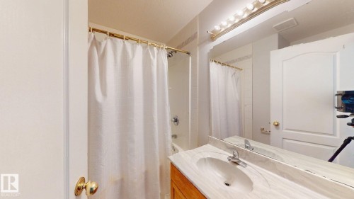 Bright bathroom featuring a vanity with an integrated sink, polished chrome faucet, and full-width mirror with overhead vanity lighting - 3738 28A Street, Edmonton, AB 